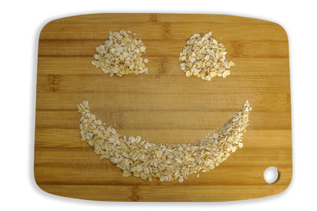 Oatmeal is laid out in a patterned smile pattern on a wooden cutting board. Isolated photo with shadow on white backgroundの写真素材