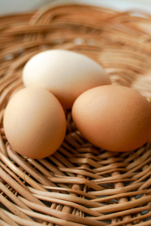 Three chicken eggs of different colors and different sizes lie in a wicker basket. Photo combined, blurred backgroundの写真素材