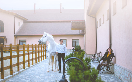 Man and woman with the white horse stay on the horses club backgroundの写真素材