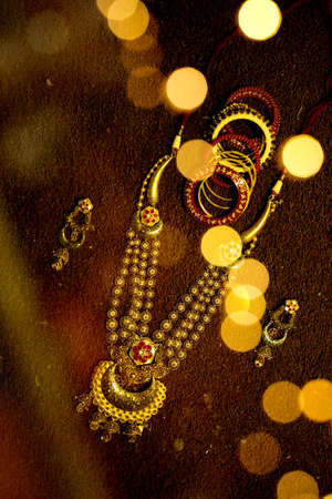gold jewellery golden necklace(haar) bracelets butti dark background with bokeh bride getting ready for beauty parlour beautiful ornamentsの写真素材