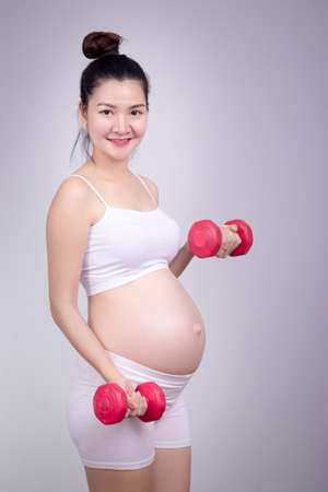 Pregnant exercises concept.A portrait of a Beautiful asian pregnant woman doing light exersice by using dumbell at home.の写真素材
