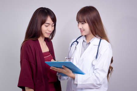 Female Asian doctor holding application form while consulting patientの写真素材