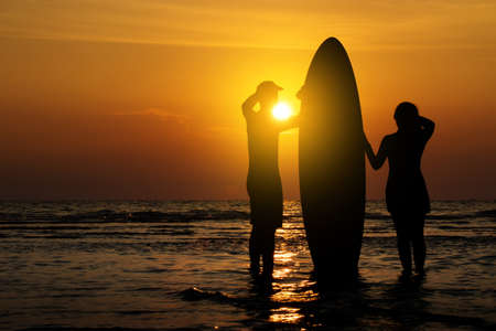 Man and girl with surfboard on the beach at sunsetの写真素材