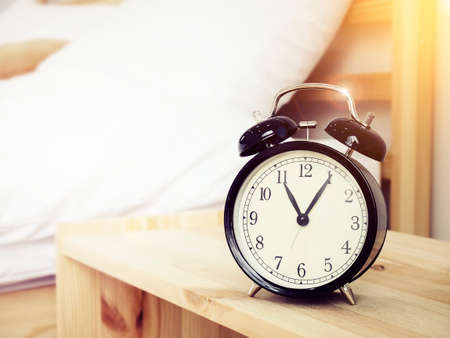 Closeup retro alarm clock on Bedside table with bed background and copy space, retro styleの写真素材