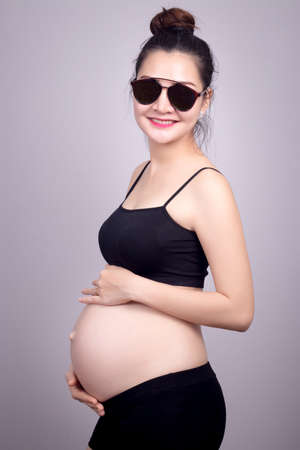 Happy mom concept : Portrait of happy pregnant Asian woman with smile face in black dress with sun glasses. Beautiful Asia female model in her 20s.の写真素材