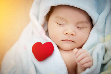 Family love relationship concept : red heart shaped put on sleep cute Asian baby. Lovely newborn Asia infant model female in her first yearの写真素材