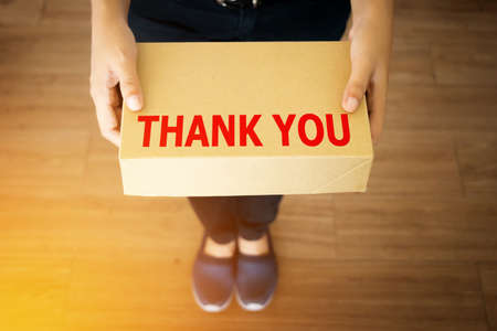 Thank you message for customer who shopping with your shop concept : Thank you message word on simple delivery brown box in hand of friendly sender manの写真素材