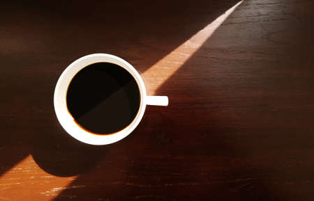 White ceramic coffee cup with espresso black coffee on wooden table background with triangle sun light and shade from window, top viewの写真素材