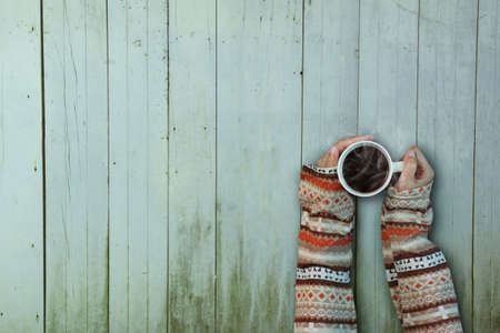 Female hands holding cup of coffee on rustic wooden table backgroundの写真素材
