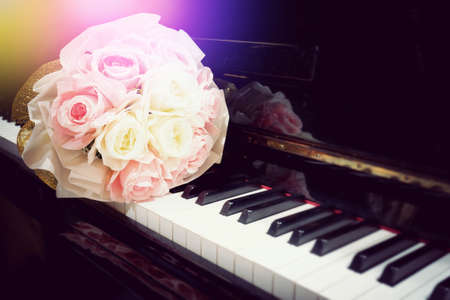 Rose flower in bouquet on keyboard of piano with light flare in concert performance. Selective focus image. Warm color tone music backgroundの写真素材