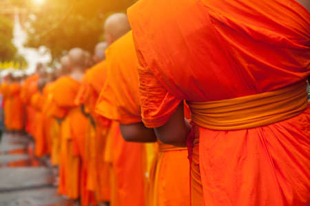 Buddhist philanthropy concept. Buddhist Monks line up in row waiting for Buddhism people to give alms bowl in Thai temple at morning time. Selective focus at front Monk. Light with len flare effectの写真素材