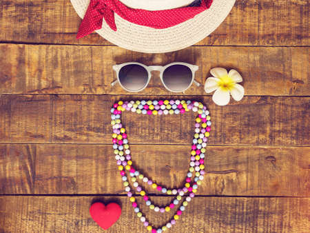 flat lay of hat , necklace , sunglass , flower and red heart shape as traveler's accessories items for summer vacation on wooden background with copy space. love travel and vacation for girl ,womanの写真素材