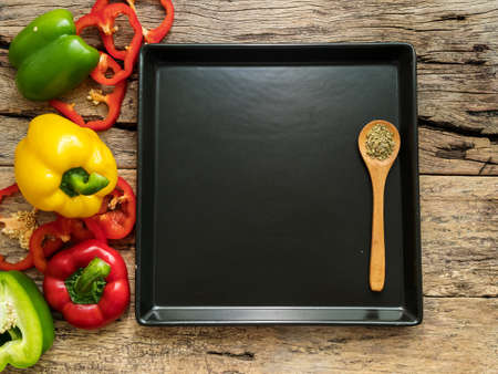 flat lay of empty blank black plate with wooden spoon and utensils with herbs and colorful bell...