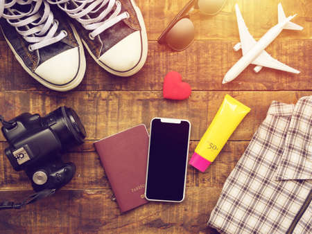 flat lay of passport ,mobile, plane model , sneakers , wallet , camera and traveler's accessories items on wooden background with copy space. travel and vacation conceptの写真素材