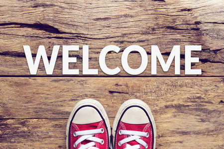 welcome sign text on wooden floor with red sneaker on itの写真素材