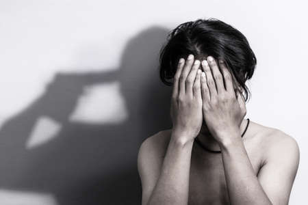 man with depression sitting head in hands with shadow of gun that was pointing his head, thinking to...