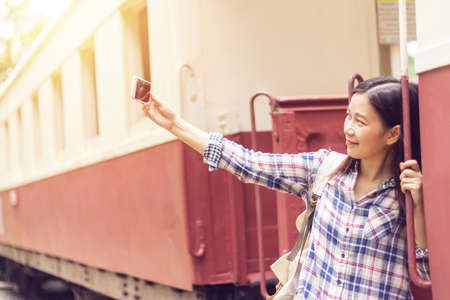 happy young Asian traveller woman taking selfie photo from mobile phone at train station while travelingの写真素材