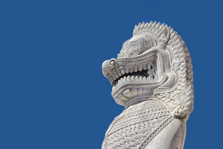 sculpture of ancient white stone singha statue isolated on blue sky background in front of temple in...