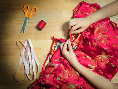 top view of cropped female hands sewing Cheongsam dress with needle at seamstress workplace with sewing equipmentの写真素材