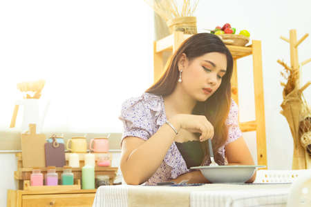 lonely Asian woman sit at the table eating meal in the kitchen alone in the morning with beautiful...