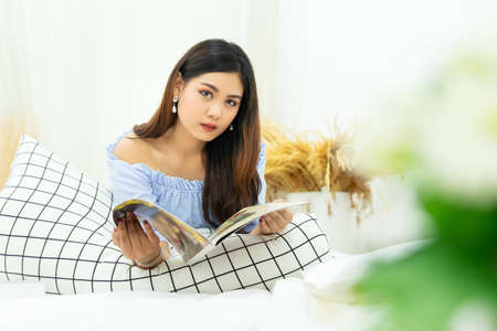 beautiful Asian woman lying on white cozy bed reading a book enjoys of rest at comfort homeの写真素材
