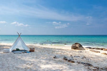 romantic white picnic tent on white sand beach with crystal clear water and blue sky at background