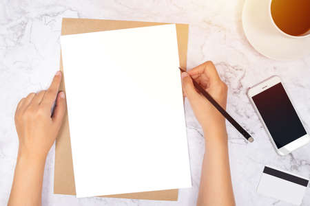 flat lay of woman hand writing in a blank white paper on brown paper envelope with pencil ,mobile...