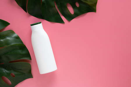 cosmetic nature skincare concept. white cosmetic bottle container with blank label for branding mock up, decorate with green tropical leaves on pink background with copy spaceの写真素材