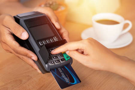 close up of hand entering credit card pin code for security password in credit card swipe machine at point of sale terminal in shop during shopping timeの写真素材