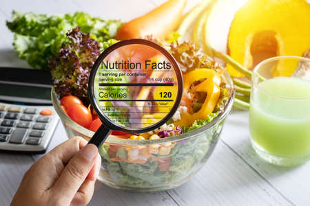 nutritional information concept. hand use the magnifying glass to zoom in to see the details of the nutrition facts from food , salad bowlの写真素材