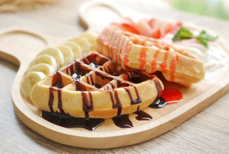 tasty waffle topped with strawberry syrup and chocolate sauce, side dishes are fresh strawberry...