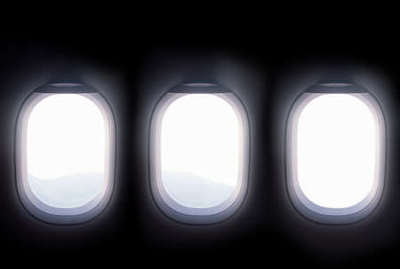 three airplane windows open white window shutter wideout to view of mountain hilltop during travel by airの写真素材