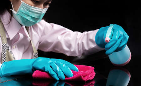 woman wear a hygienic mask , use blue rubber glove holding pink microfiber cleaning cloth and spray bottle with sterilizing solution make cleaning and disinfected for good hygieneの写真素材