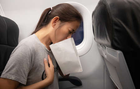 female passenger on the plane felt airsick, affected with nausea due to travel in an aircraft using air sickness bag for vomiting due to airsicknessの写真素材