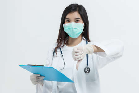 young Asian doctor woman wearing doctor gown uniform coat , medical mask and stethoscope holding a clipboard looking unhappy and angry showing rejection and negative with thumb down gesture.の写真素材