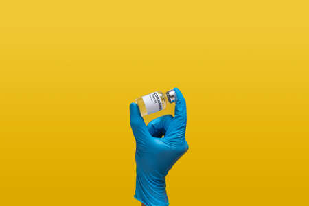 doctor at laboratory wearing blue rubber glove holding Coronavirus vaccine dose bottle label, isolated on yellow background. laboratory analyzing for testing and invent drug and vaccine for covid-19の写真素材