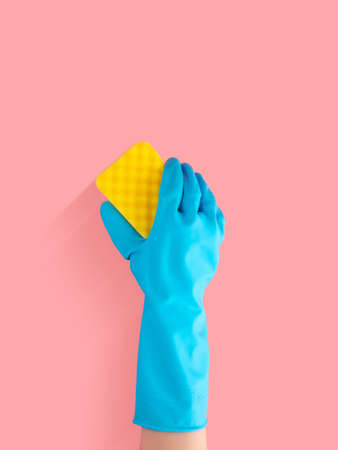 hand in blue rubber glove holding yellow cleaning sponge, cleaning and disinfection for good hygiene isolated on pink background with copy space for textの写真素材