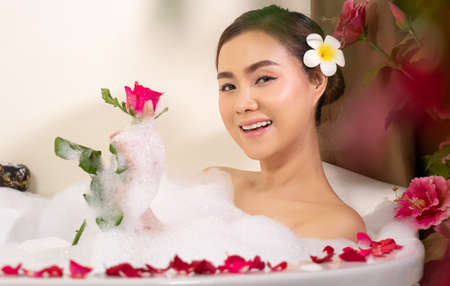 relaxing beautiful Asian woman pampering her body in water in a spa bathtub with white foam bubble...