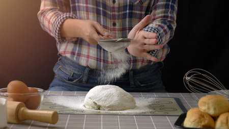 artisan bread working with dough. Use a sieve to sift flour into dough handmade bread with bakery equipment tools, black background. Bread-making process for baker at work.の写真素材