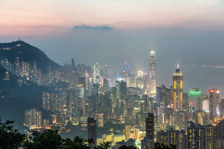 Hong Kong skyline shot after sunset from the top of a mountain in Hong Kong island. The view goes through the Victoria harbor until Kowloon.の写真素材
