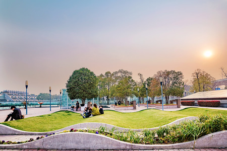 Shanghai, China, March 07, 2016:  People sitting on the grass and talking outside Shanghai South Railway station during sunsetのeditorial素材