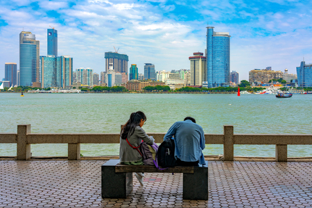 XIAMEN, CHINA -OCTOBER 12: People sitting at the waterfront area of Gulangyu with Xiamen city skyline in the distance on October 12, 2018 in Xiamenのeditorial素材