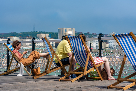BRIGHTON, UNITED KINGDOM - JULY 24: People sitting on deck chairs on Brighton pier in the summer time on July 24, 2019 in Brightonのeditorial素材