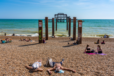 BRIGHTON, UNITED KINGDOM - JULY 24: People sunbathing on Brighton Beach by the old ruins of the West Pier on July 24, 2019 in Brightonのeditorial素材
