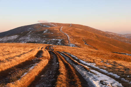 Autumn landscape in the Carpathian mountains. Dirt road with snow on the Borzhava ridge. Sunset...