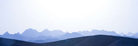 Desert landscape in blue color. Stony hills in the foreground with the silhouette of rocky mountains. Space, fantastic atmosphere in the sahara desertの写真素材