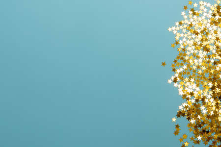 Star shaped shining golden confetti on light blue background. Sparkle sequins. Festive design,...