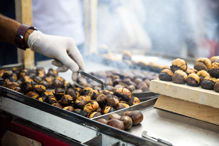 Street food. Cooking of hot roasted chestnuts. Chefs hand in disposable gloves with tongsの写真素材