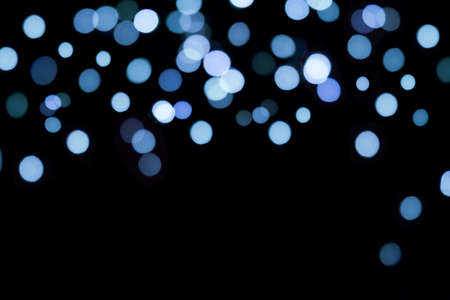 Bokeh blue lights background. Blurred festive Christmas lights on a black backgroundの写真素材