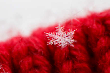 Extreme macro photo of snowflake on red knitwear. Selective focus. Texture of fabric and threads. Geometric unique structure of a snowflake on a frosty day. Winter backgroundの写真素材